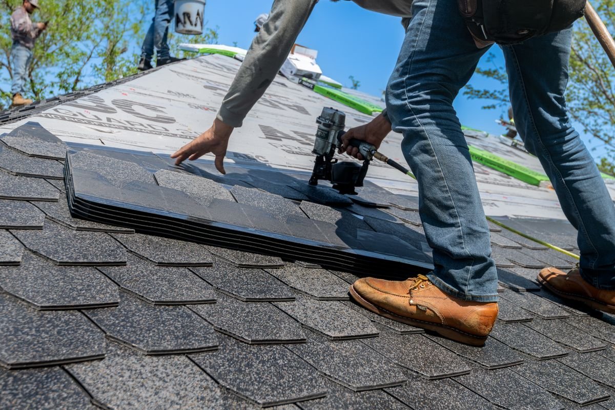Roofer using a nail gun to install asphalt shingles on a residential roof — an AI receptionist for roofing companies answers the calls roofers can't take on the job