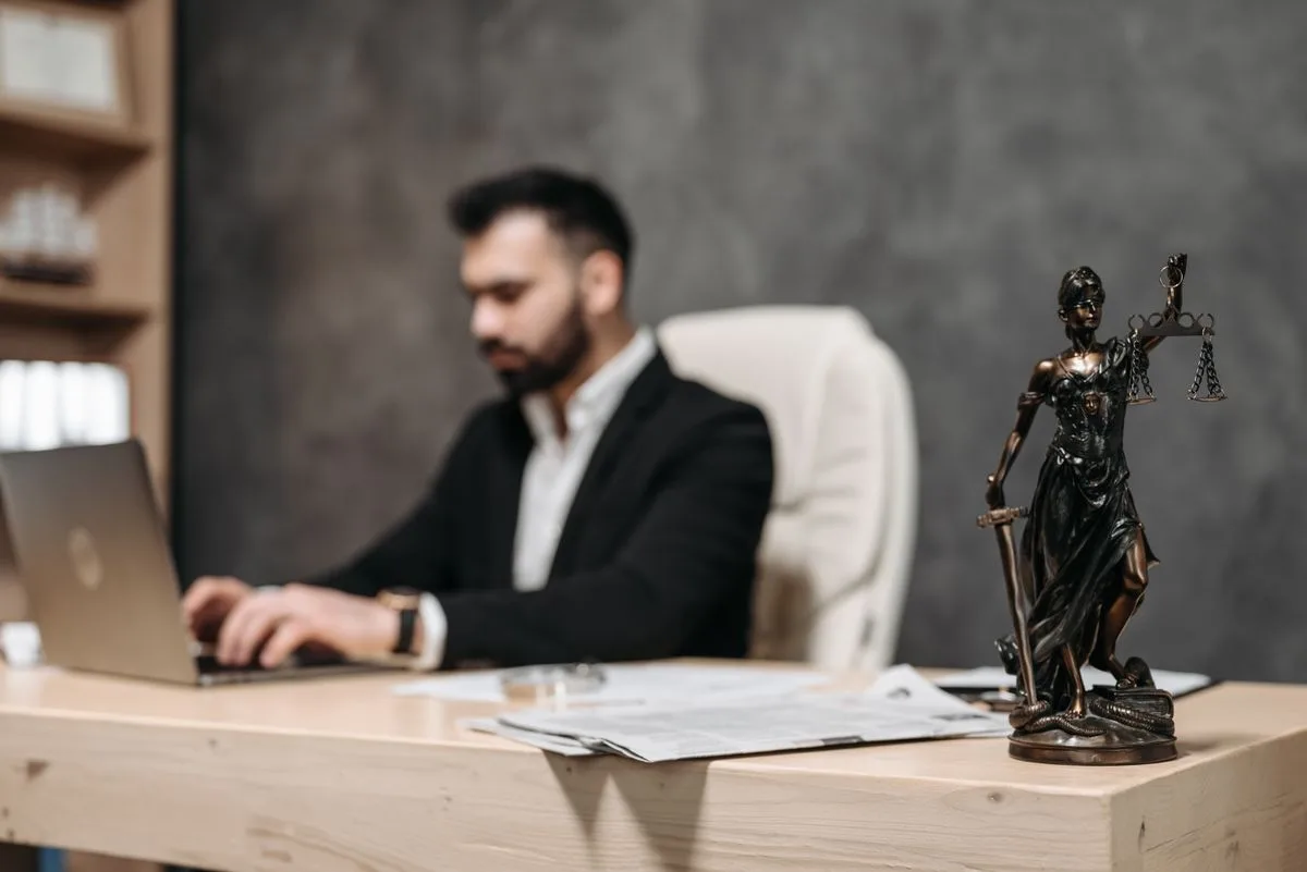A businessman working on a laptop with a Lady Justice statue on the desk — comparing the cost of an AI receptionist for law firms against a full-time hire