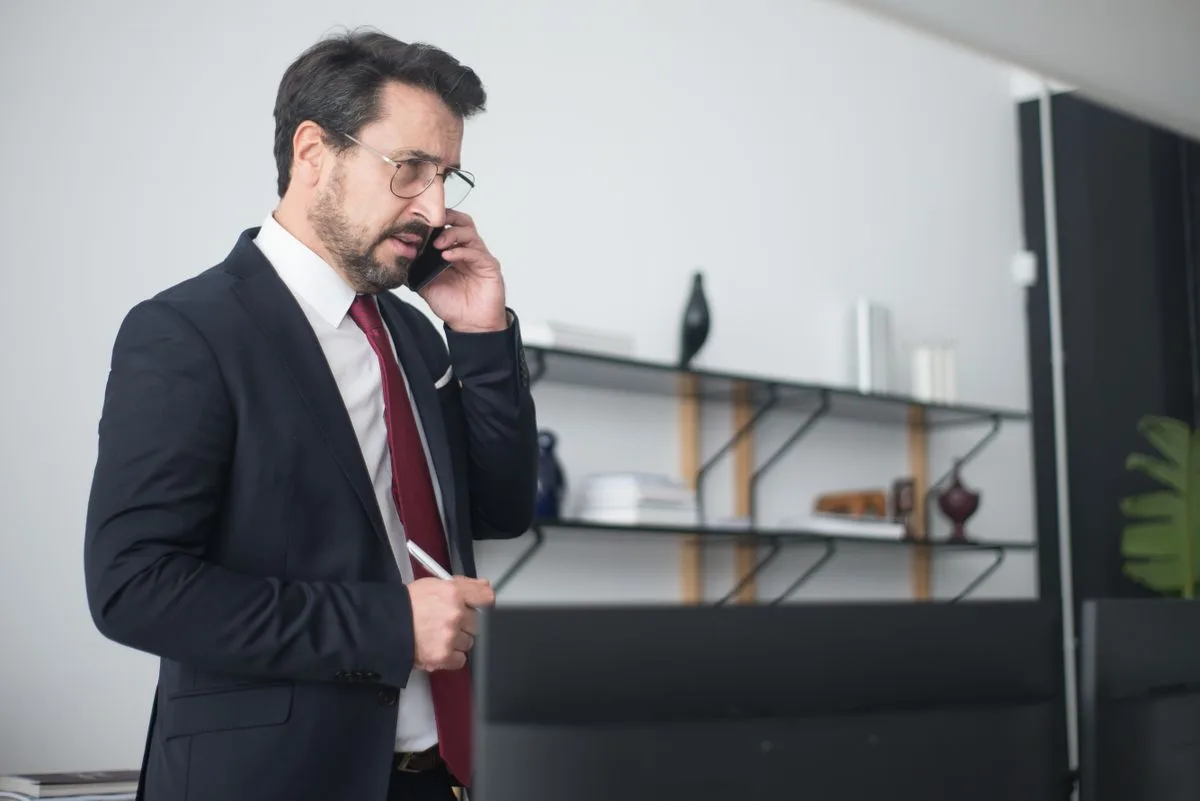 Businessman in a suit speaking on a mobile phone in a modern office — unanswered calls are how law firms lose new clients