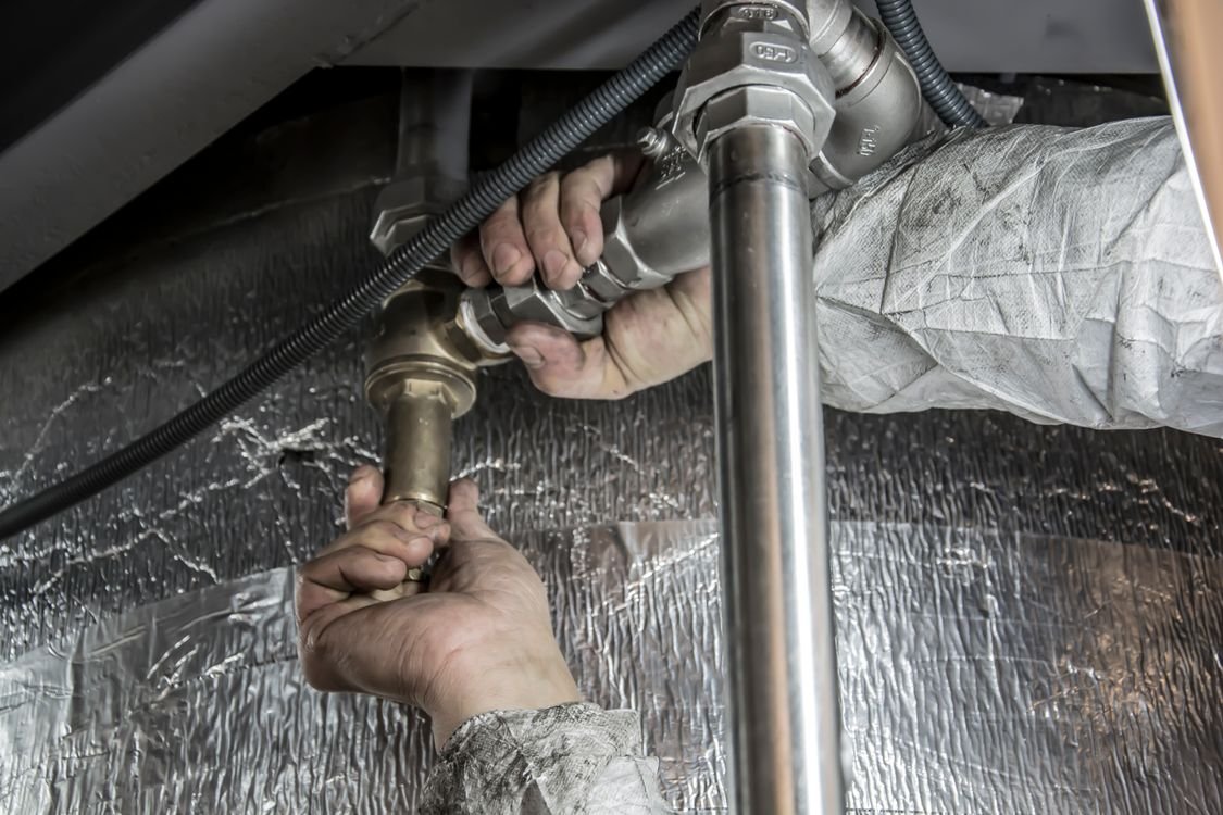 Close-up of a plumber's hands installing steel pipes indoors — the skilled hands-on work that stays human even with an AI receptionist answering the phones