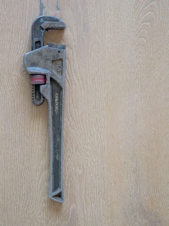 Close-up of a plumber's wrench on a wooden surface — weighing what an AI receptionist for plumbers costs against a full-time hire