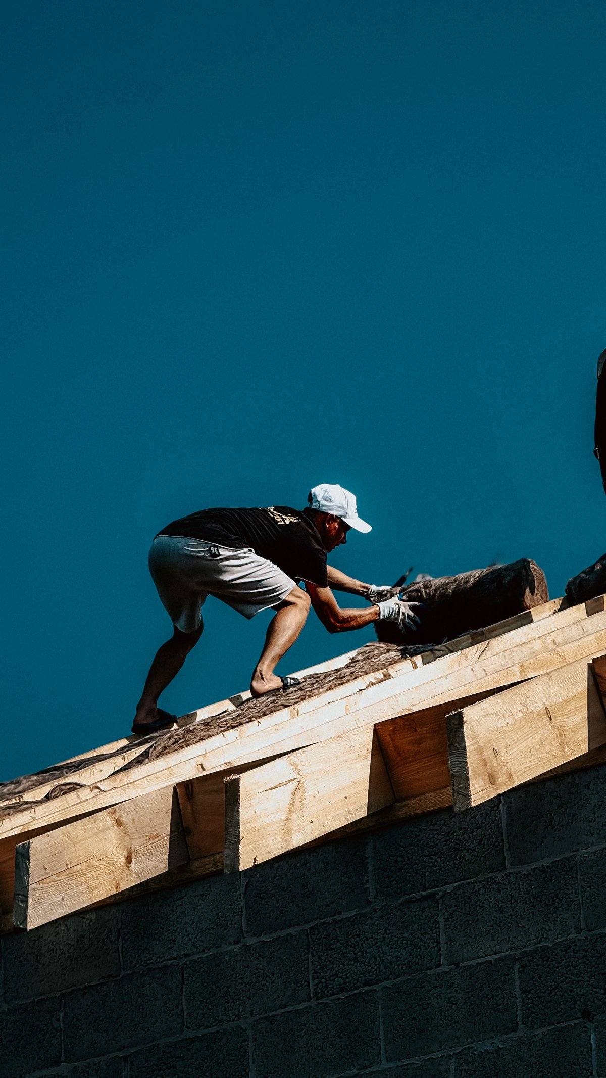 Roof construction worker in action against a clear sky — comparing the cost of an AI receptionist for roofing companies with a full-time hire